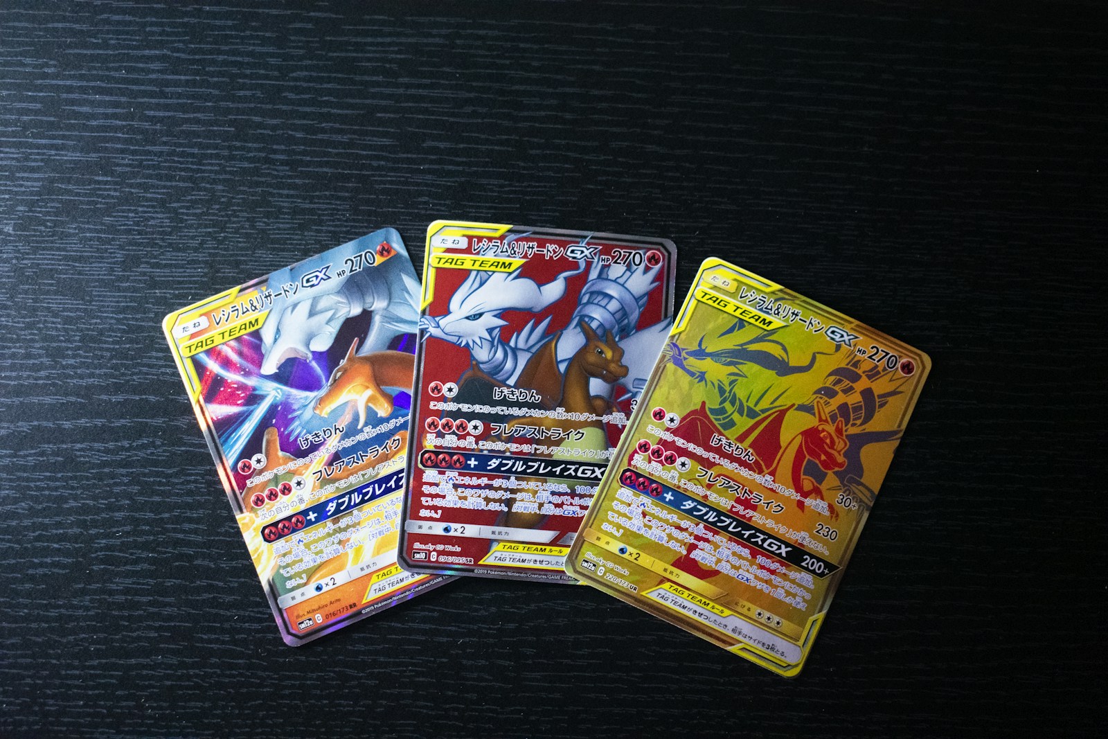 Three Japanese Reshiram and Charizard GX cards with different artwork arranged on a dark tabletop.