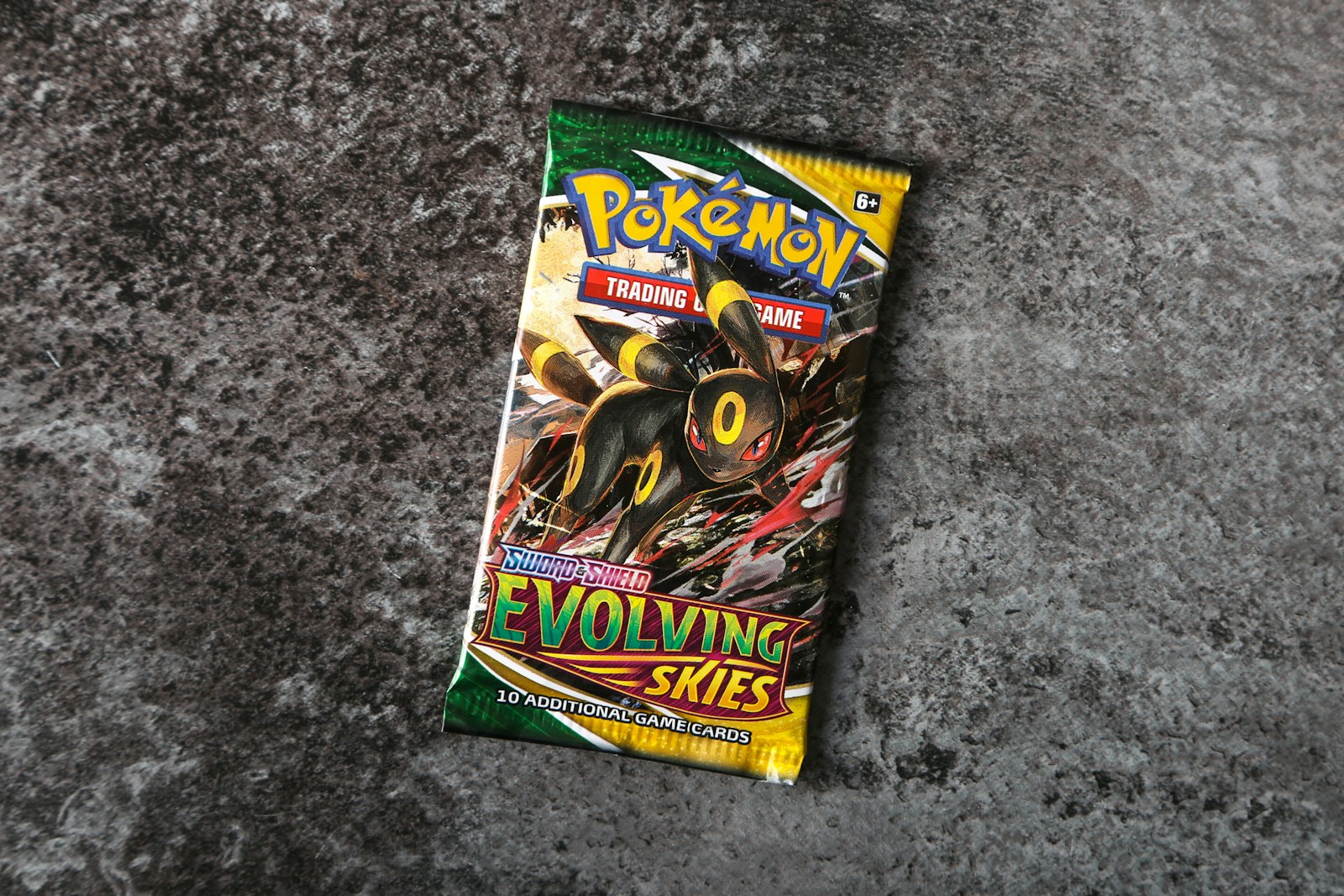 An English Pokémon Evolving Skies booster pack with Umbreon artwork lying on a gray stone surface.